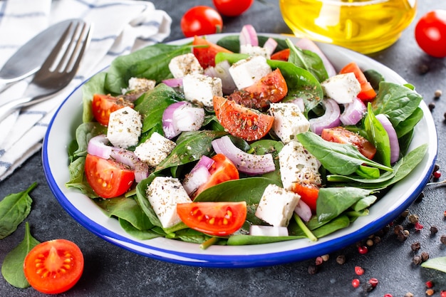 La nourriture saine. Salade grecque aux épinards, tomate, poivron, oignon rouge, fromage feta sur fond de béton foncé