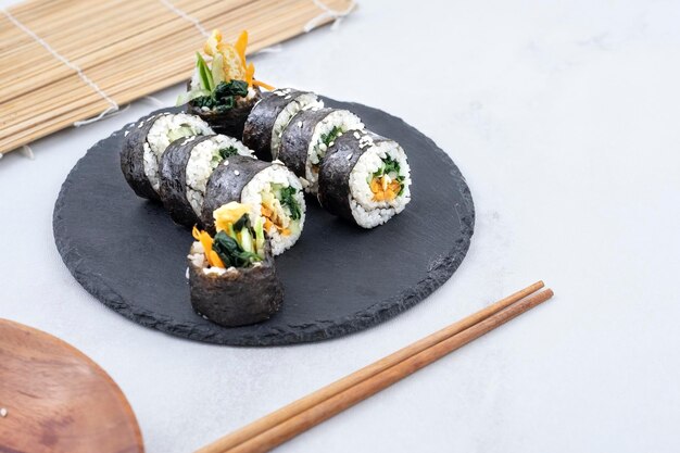 La nourriture sud-coréenne appelée kimbap servie sur une assiette plate en pierre et des baguettes sur le côté