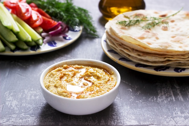 Nourriture végétalienne, houmous fait maison avec pain plat, légumes et huile d'olive sur un fond en béton.