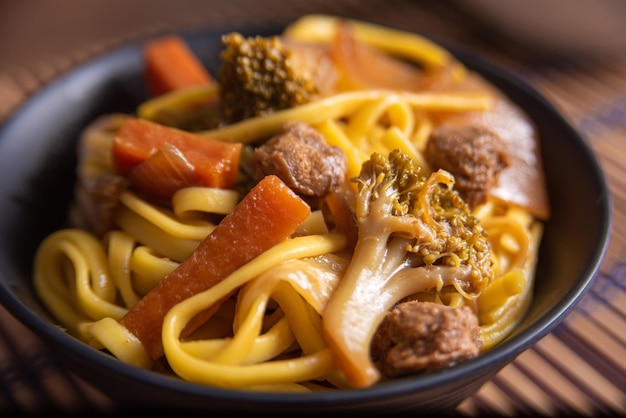 Nourriture végétalienne Vegan Yakisoba avec des baguettes dans un bol sur une natte de bambou sur une mise au point sélective en bois