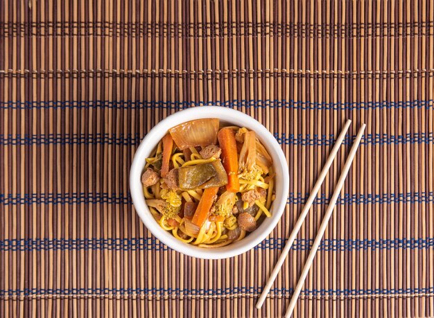 Nourriture végétalienne Vegan Yakisoba avec des baguettes dans un bol sur une natte de bambou sur la vue de dessus en bois