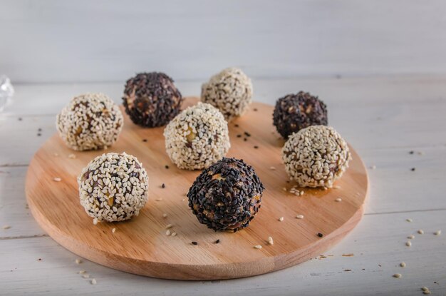 Nourriture végétarienne, boules d'énergie maison de noix, dattes, pruneaux, canneberges et miel avec sésame blanc et noir sur fond blanc. Espace de copie