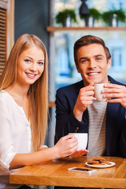 Nous aimons passer du temps ensemble. Beau jeune couple regardant la caméra et souriant tout en dégustant un café au café ensemble