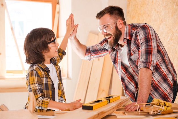 Nous l'avons fait! Joyeux jeune charpentier et son fils se donnant un coup de main tout en travaillant en atelier