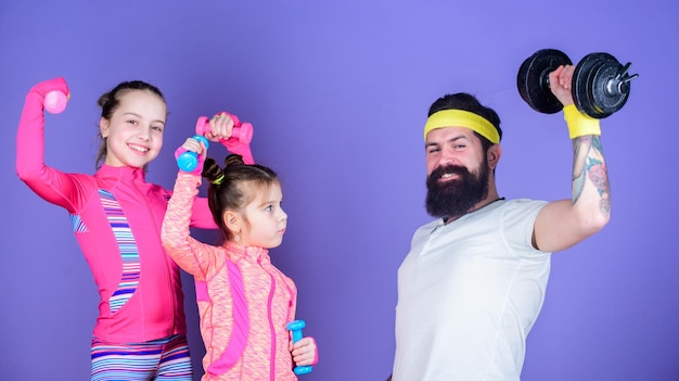 Nous faisons de l'exercice tous les jours Père et filles en cours de gym Entraînement familial heureux en cours de gym Père et enfants s'entraînant au gymnase Entraîneur sportif et petites filles renforçant leur force avec des haltères