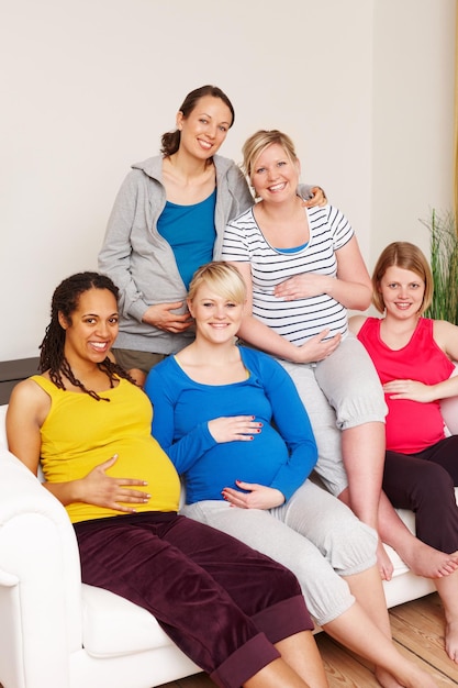 Nous ne pouvons pas attendre le grand jour Un groupe de femmes enceintes multiethniques assises sur un canapé et souriant à la caméra