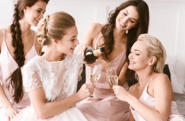 Photo nous nous amusons ensemble. agréable ravi de jeunes filles assises dans la chambre blanche tout en s'amusant et en buvant de l'alcool