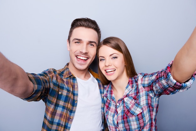 Nous sommes beaux! Heureux jeune couple d'amoureux faisant selfie en se tenant debout sur fond gris