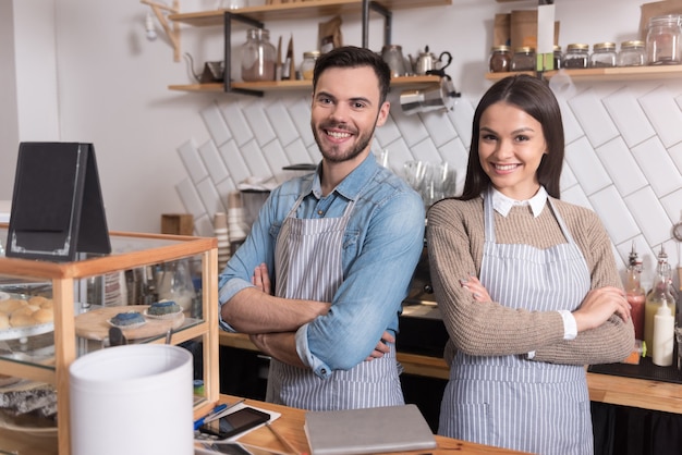 Nous sommes forts ensemble. Heureux jeune couple croisant les mains sur la poitrine et souriant tout en se tenant derrière le bar.