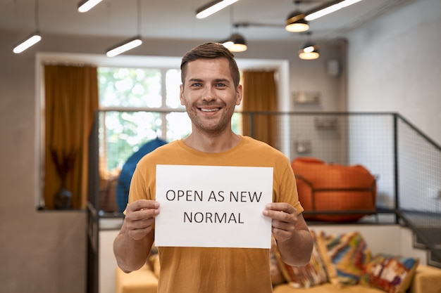 Nous sommes ouverts jeune employé de bureau homme heureux montrant du papier avec du texte ouvert comme nouveau normal et souriant à