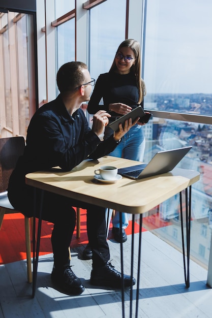 Nous travaillons ensemble sur un projet d'entreprise Deux jeunes collègues travaillent sur un ordinateur portable dans un grand bureau moderne Partenaires commerciaux au bureau au travail