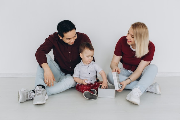 Nouveau bâtiment résidentiel maison achat concept d'appartement. Famille multiculturelle avec fils assis sur le sol, maman caucasienne et papa asiatique avec leur fils