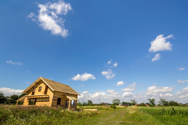 Nouveau chalet écologique en bois non fini à partir de matériaux naturels en construction dans un champ vert sur un village lointain et un fond d'espace de copie de ciel bleu. Traditions anciennes et concept de construction moderne.