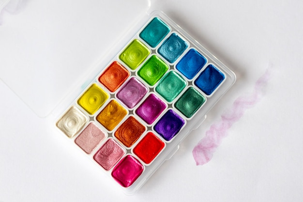 Un nouveau coffret d'aquarelles multicolores en coffret blanc Une pointe d'aquarelle rose près de la palette