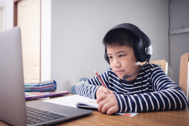 Un nouveau garçon asiatique normal étudie en ligne en regardant l'écran de l'ordinateur portable sourire heureux et rire avec plaisir à la maison. concept d'éducation technologique, travail à domicile