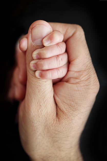 Un nouveau-né après la naissance s'accroche fermement au doigt des parents Gros plan sur une petite main d'un enfant et la paume d'une mère et d'un père Le concept d'éducation, de garde d'enfants et de soins de santé