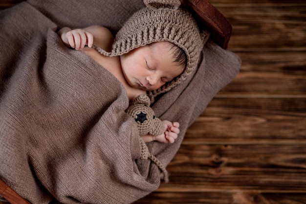 Nouveau-né, beau bébé se trouve et tenant un petit ours en peluche dans le lit sur fond de bois, espace copie