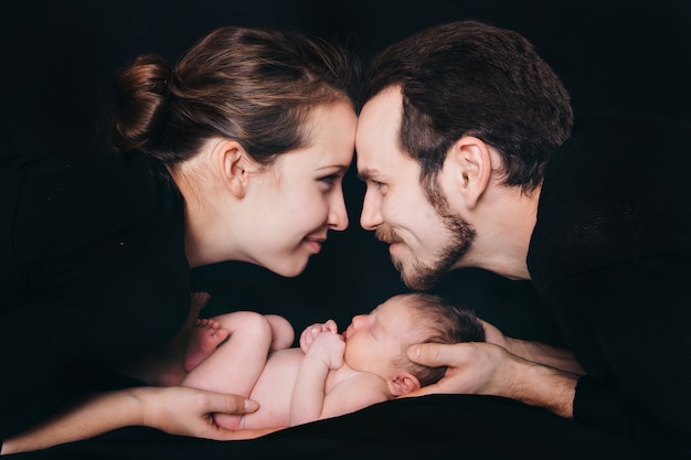 Nouveau-né couché sur les mains des parents sur fond noir. Imitation d'un bébé dans l'utérus.