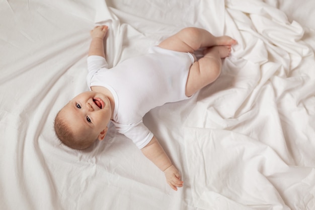 nouveau-né dans un body blanc est allongé sur le dos sur un tissu blanc vue de dessus produits pour enfants