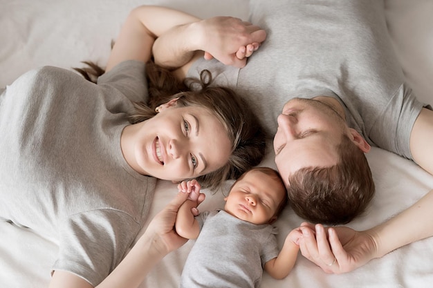 Nouveau-né dans les bras de la mère et du père sur le lit Carte postale Fête des mères et des pères Journée de la protection des enfants Journée mondiale du bonheur Enfant souriant Parentalité heureuse