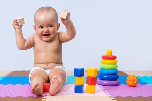 Un nouveau-né joyeux dans la salle de jeux est assis sur le sol et tient des cubes de bois dans ses mains