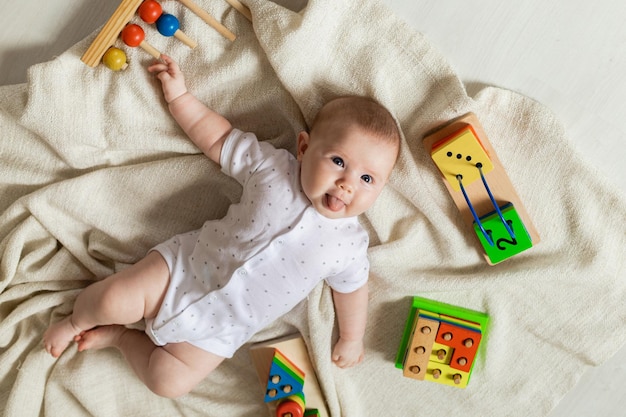 Un nouveau-né mignon dans des vêtements légers joue avec des jouets éducatifs allongés sur le sol sur une couverture en lin gris. vue de dessus. produits pour enfants. enfance et maternité heureuses. espace pour le texte