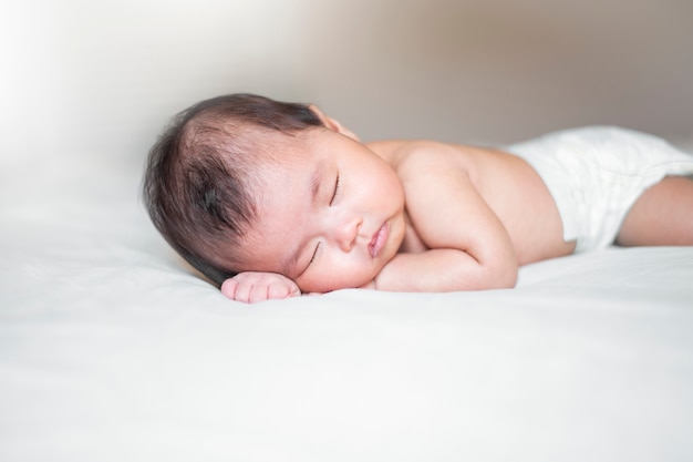 Nouveau-né mignon dort sur un lit blanc