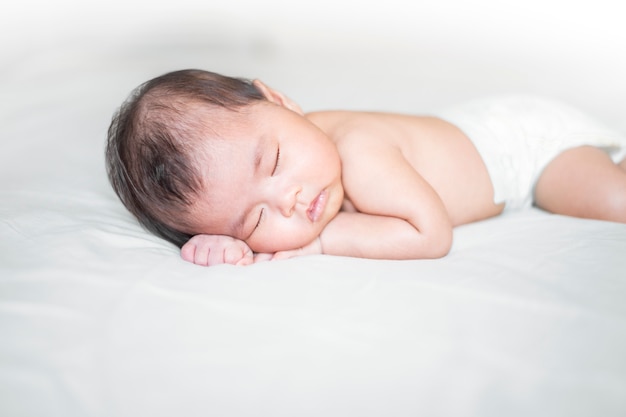 Nouveau-né mignon dort sur un lit blanc