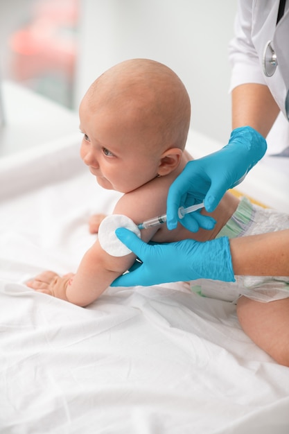 Nouveau-né mignon tranquille dans une couche injectée par un professionnel de la santé dans des gants jetables en nitrile