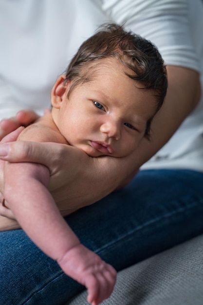 Un nouveau-né se trouve dans les bras de sa mère, seules ses mains sont visibles, le bébé est en gros plan