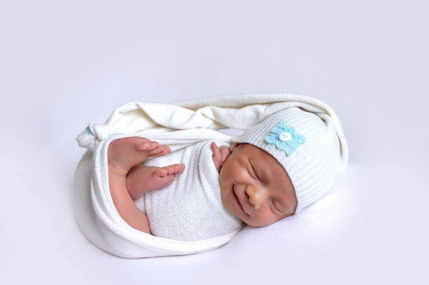 Nouveau-né souriant dans un rêve sur fond blanc dans un bonnet de sommeil