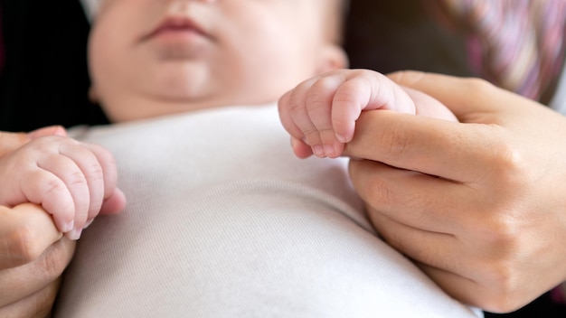 Le nouveau-né tient un doigt de mère sur fond de lit de drap blanc Un bébé