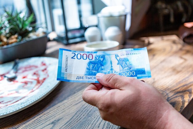 Photo de nouveaux billets russes libellés en 2000 roubles dans une main masculine, il va payer la facture dans un restaurant