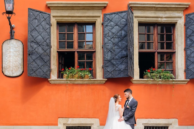 Les nouveaux mariés amoureux se tiennent sous les fenêtres d'une maison orange