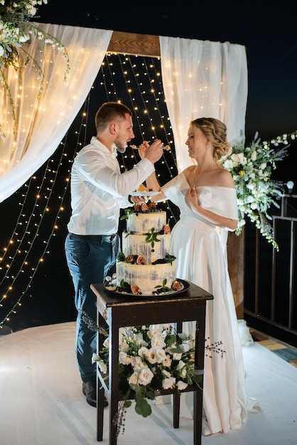 Les nouveaux mariés coupent joyeusement le rire et goûtent le gâteau de mariage