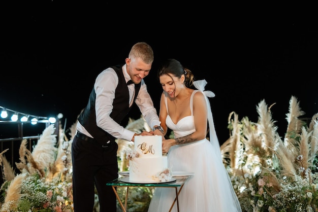 Les nouveaux mariés coupent joyeusement le rire et goûtent le gâteau de mariage