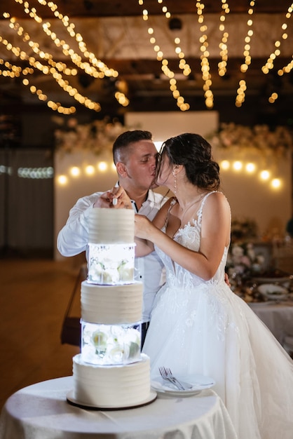 Les nouveaux mariés coupent joyeusement le rire et goûtent le gâteau de mariage