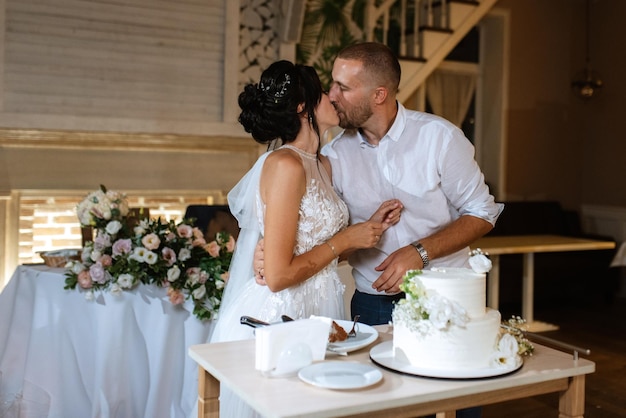 Les nouveaux mariés coupent joyeusement le rire et goûtent le gâteau de mariage