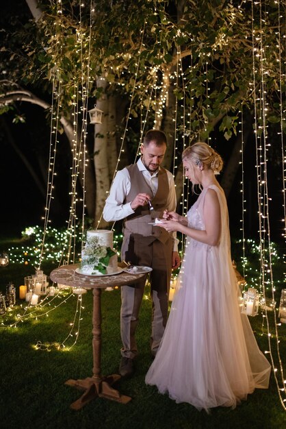 Les nouveaux mariés coupent joyeusement le rire et goûtent le gâteau de mariage