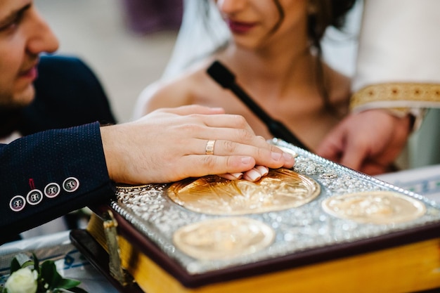 Les nouveaux mariés se tiennent la main lors de la cérémonie de mariage à l'église Le prêtre bénit la sainte bible pour une longue vie aux mariés