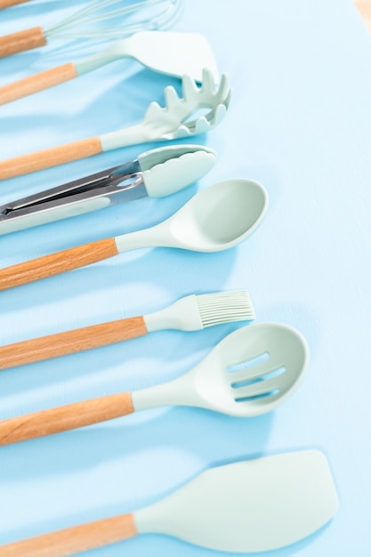 Nouveaux ustensiles de cuisine en silicone bleu avec poignées en bois sur fond bleu.