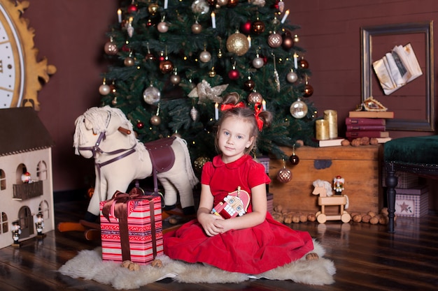 Nouvel An 2020. Joyeux Noël, Joyeuses Fêtes. Petite Fille En Robe Rouge Est Titulaire D'un Jouet Casse-noisette En Bois Vintage Près D'un Arbre De Noël Classique à La Maison. Ballerine Avec Le Casse-noisette Le Soir Du Nouvel An.