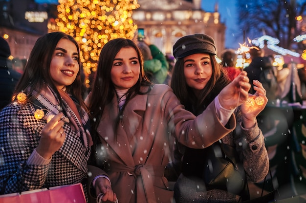 Nouvel an. Amies de femmes brûlant des cierges magiques à Lviv par arbre de Noël sur une foire de rue célébrant les vacances Filles heureuses s'amusant sous la neige. Fête