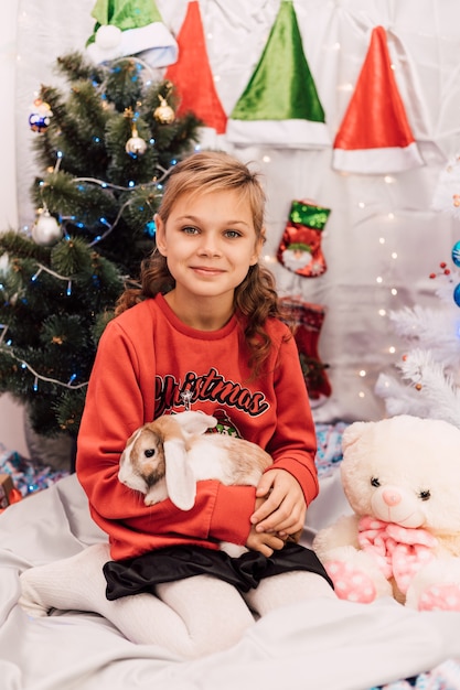 Nouvel An une fille dans un pull du Nouvel An tient un lapin près de l'arbre de Noël