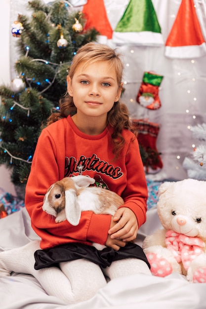 Nouvel An une fille dans un pull du Nouvel An tient un lapin près de l'arbre de Noël