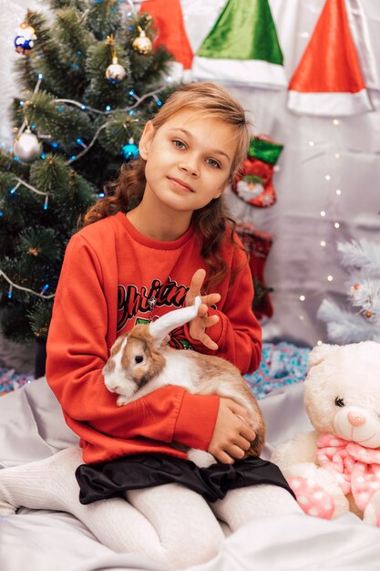 Nouvel An une fille dans un pull du Nouvel An tient un lapin près de l'arbre de Noël