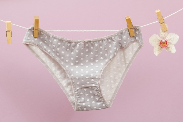 Nouvelle culotte sur corde à linge avec pinces à linge et fleur d'orchidée sur fond lilas