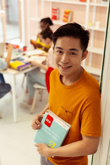 Nouvelle édition. Joyeux jeune homme gardant le sourire sur son visage tout en posant devant la caméra