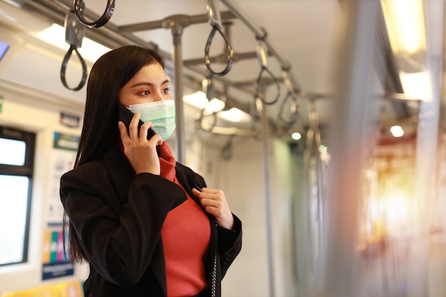 Nouvelle épidémie normale de covid-19, jeune femme d'affaires asiatique portant un masque de protection pour prévenir l'infection par le virus covid-19 ou le coronavirus des personnes en train, en utilisant la communication par smartphone en train