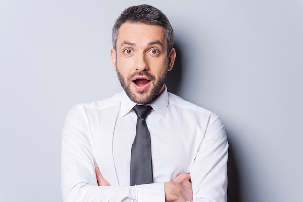 Une nouvelle incroyable ! Portrait d'un homme mûr surpris en chemise et cravate gardant la bouche ouverte et regardant la caméra en se tenant debout sur fond gris